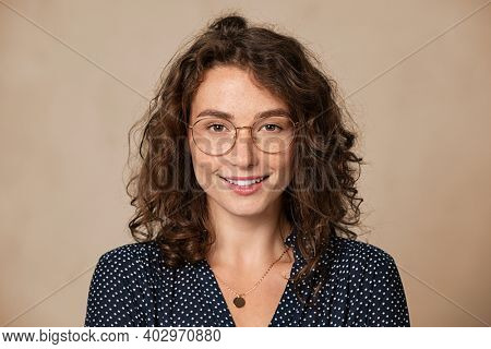Young woman wearing eyeglasses isolated on beige background and looking at camera. Proud female student with nerd glasses isolated on wall. Sophisticated glamour girl in shirt wearing big spectacles.