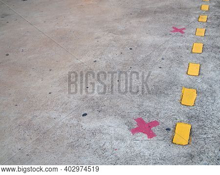 red paint cross marks on cement floor of train station platform with yellow dividing line, symbol for passengers stand to wait for train and keep distance to prevent spread of covid-19