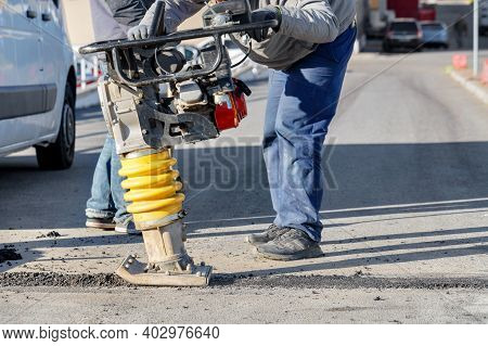 Road Workers Use A Petrol Vibratory Rammer To Pave A Small Section Of Road On A Bright Sunny Day, Se