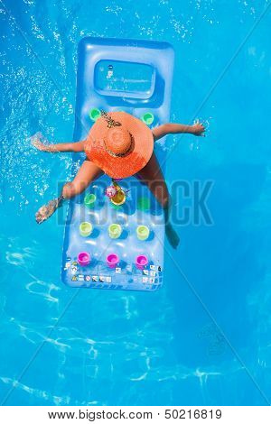 Young woman with straw hat and pineapple fresh cocktail on a lilo in the swimming pool