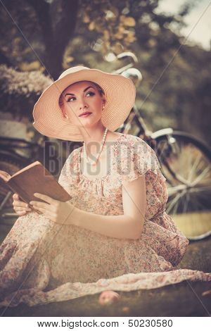 Blond beautiful retro woman reading book on a meadow 