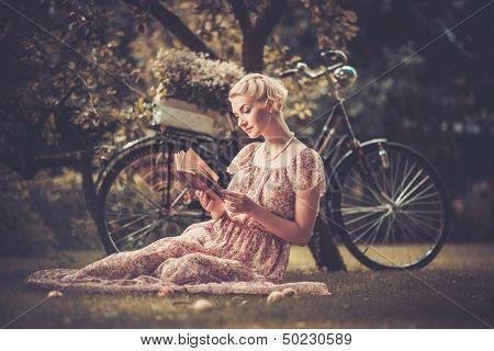 Blond beautiful retro woman reading book on a meadow 
