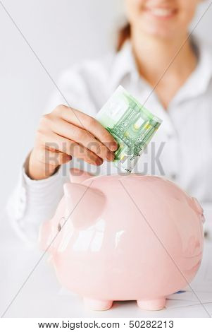 Geschäft, Büro, Haushalt, Schule, Steuern und Bildung Konzept - Frau setzt Euro-Bargeld in großen Schwein