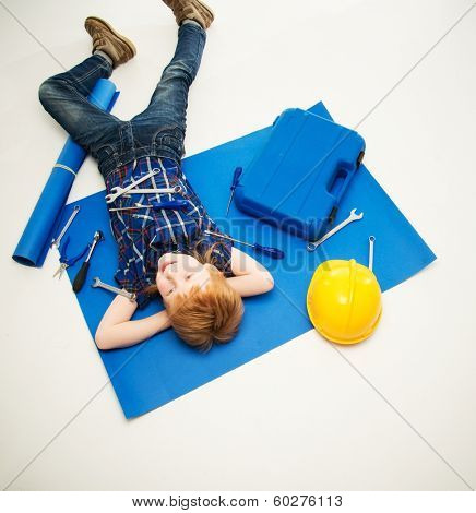 Funny little mechanic boy with wrench tools lying on a blueprint 