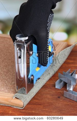 Fastening fabric and board using construction stapler on bright background