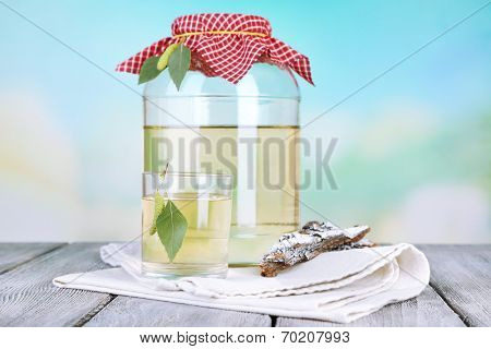 Glass and large flagon of fresh birch sap  on a wooden table on nature background