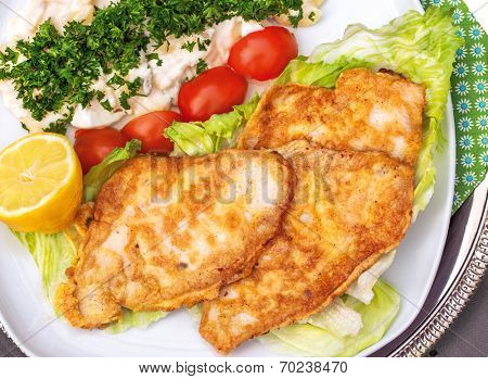 Baked plaice fillet with potato salad on a plate with tomato and salad decoration