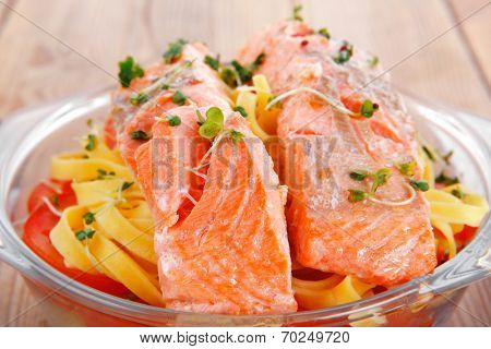 fresh fried natural pink salmon on italian traditional tagliatelle backed with tomato and vegetables served over wooden table with cutlery