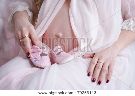 Woman hands holding baby's bootees next to the pregnant belly