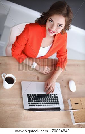 Attractive woman sitting at desk in office, working with laptop