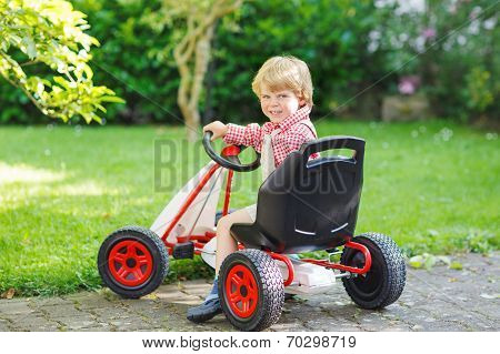 Active Little Boy Driving Pedal Car In Summer Garden