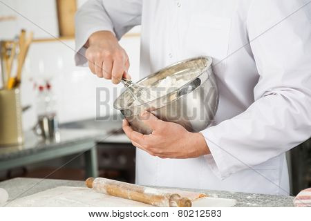 Midsection of male chef mixing batter with wire whisk in bowl at commercial kitchen counter