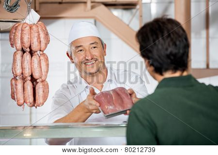 Happy mature male butcher showing packed sausages to customer at butchery