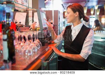 Happy barmaid using touchscreen till in a bar