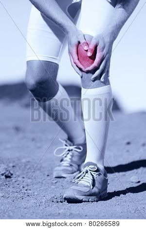Greyscale image of the legs of a sportsman with a knee injury clasping his knee depicted in red selective color conceptual of a pulled muscle, cartridge, strain, sprain or tendon injury