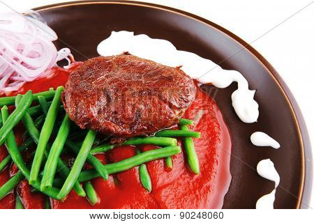 pork medallion served on tomato sauce with green peas on dark plate isolated on white background