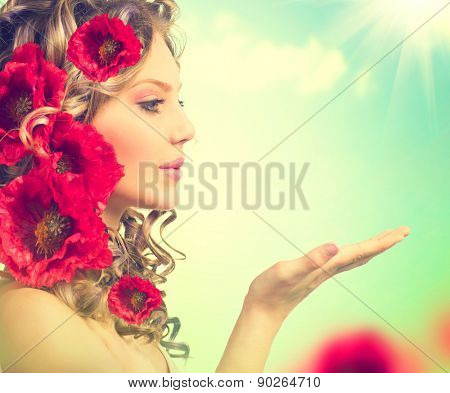 Beauty girl with red poppy flowers hairstyle and open hands. Blowing flower. Hairstyle with flowers. Fantasy girl portrait over blue sky outdoor. Summer fairy portrait. Long permed hair