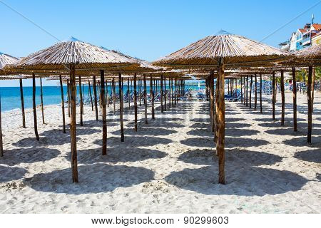 Row Of Wooden Umbrellas At Sandy Beach, Sea And Blue Sky