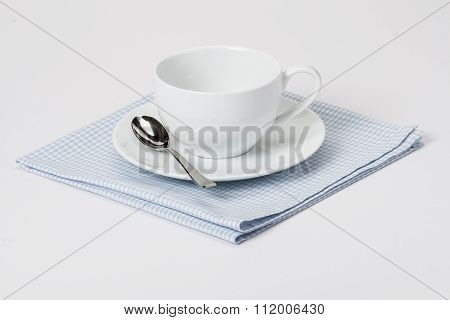 Cup, Plate And Spoon On Folded Gingham Cotton Napkin. White Back