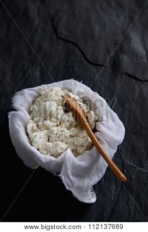 Homemade ricotta cheese draining in muslin cheese cloth on dark background