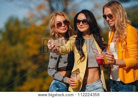 Three girls are walking in the Park in summer and drink fruit juice