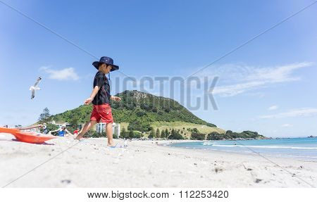 Boy In Sun Hat Walks Down Mount Maunganui Beach.