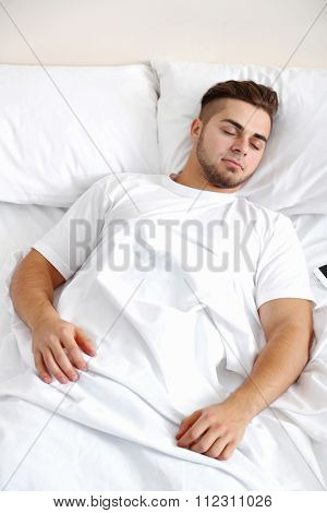 Beautiful young man snoozing on bed
