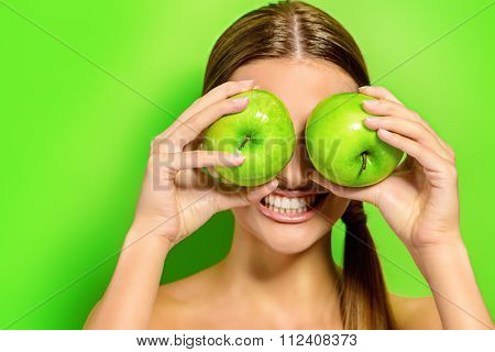 Funny laughing woman holding two gren apples before her eyes. Green background. Healthy eating concept. Diet.