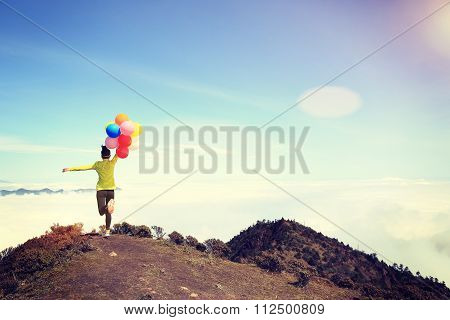 cheering young woman with colorful balloons on mountian peak
