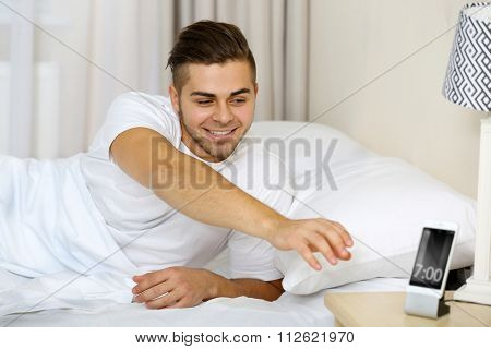 Beautiful young man waking up with mobile alarm clock
