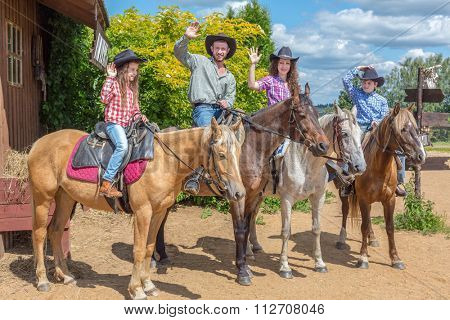 cowboy family of four on horses waving their hands