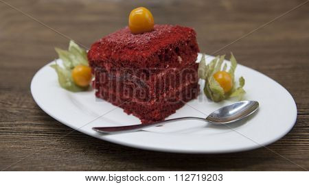 Red Velvet, fresh delicious diet cake with berry Physalis at Dukan Diet on a porcelain plate with a spoon on a wooden background.