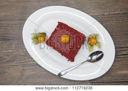 Red Velvet, fresh delicious diet cake with berry Physalis at Dukan Diet on a porcelain plate with a spoon on a wooden background.