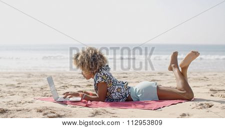 Cute african-american woman typing on a laptop on a bench
