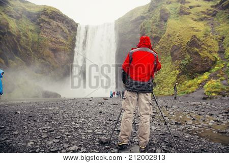 Adventurous Landscape Photographer At Waterfall. Photographing Natural Phenomenons And Beautiful Lan
