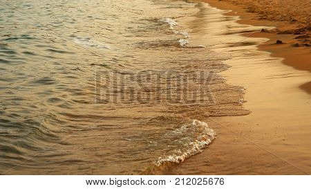 Soft sea waves rushing on the sandy beach at the sunset. The most tranquil and serene scene at the sea surf. Calm sea at night.