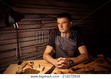 Working process of the leather belt in the leather workshop. Man holding hands on wooden table. Crafting tools on background. Tanner in old tannery. Close up men arm. Interlock fingers.