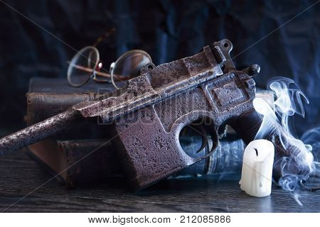 Old military pistol near extinguished candle on dark background