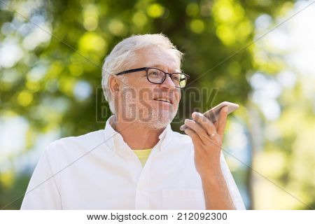 technology, senior people and communication concept - old man using voice command recorder or calling on smartphone at summer park
