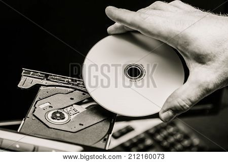 Male hand inserting a DVD into a disk drive. Black and white.