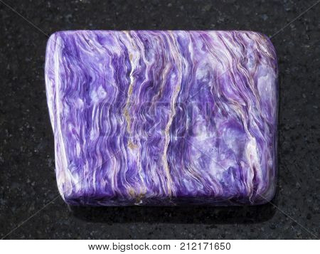 macro shooting of natural mineral rock specimen - polished slab of charoite gemstone on dark granite background from Murun Massif Yakutia Russia