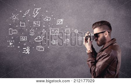 An elegant hipster guy trying to use a vintage camera with camera settings icons drawn on wall, like flash, white balace or ISO value concept