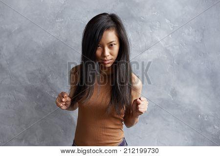 Negative human facial expressions emotions and feelings. Picture of annoyed enraged young brunette Korean woman pumping fists feeling angry staring at camera with eyes full of fury and anger