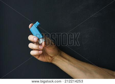 aerosol inhaler for the treatment of asthma in a male hand against a dark background.
