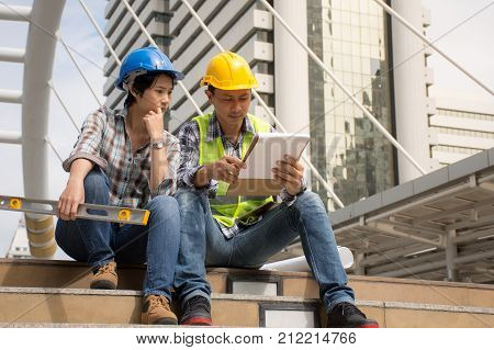 Two construction engineers working outdoors,discussing the construction in construction site with documents