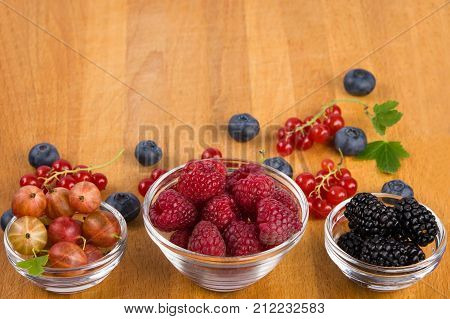 on a wooden board three plates of berries as a background