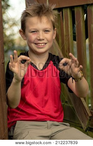 Pre-teen boy giving ok gesture sitting outside