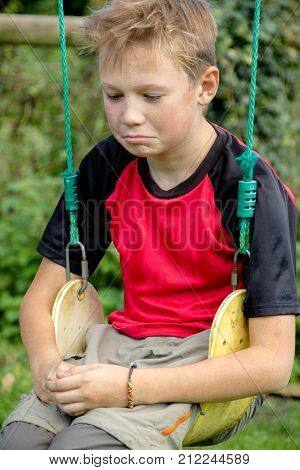 Sad pre-teen boy sitting on a swing outside