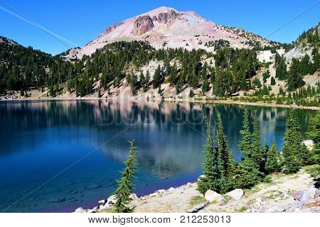 Alpine lake with dark blue water surrounded by a pine forest and mountains taken in Mt Lassen National Park, CA