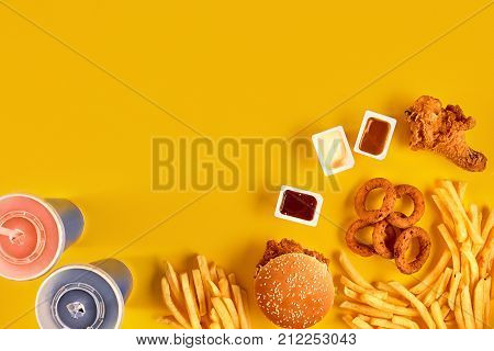 Fast food dish top view. Meat burger, potato chips and wedges. Take away composition. French fries, hamburger, mayonnaise and ketchup sauces on yellow background. Menu or receipt background. Top view. Copy space. Still life. Flat lay.